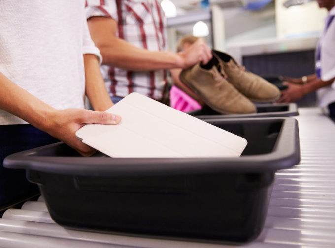 Passengers placing electronic device and shoes in bins at commercial airport security checkpont.